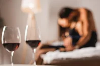 Selective focus of wedding ring on wallet near smartphone and glasses of wine with shirtless man embracing woman on bed<!-- NICAID(16103872) -->