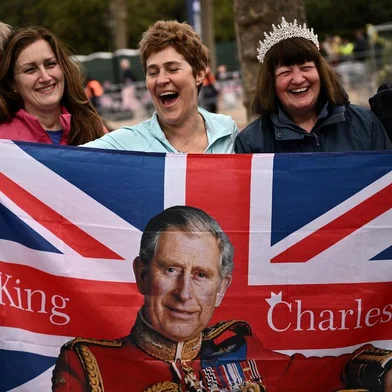 Royal fans pose with a Union Jack flag depicting Britain's King Charles III  along the procession route, on The Mall, near to Buckingham Palace in central London, on May 5, 2023, ahead of the coronation weekend. - The country prepares for the coronation of Britain's King Charles III and his wife Britain's Camilla, Queen Consort on May 6, 2023. (Photo by Marco BERTORELLO / AFP)<!-- NICAID(15420691) -->