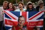 Royal fans pose with a Union Jack flag depicting Britain's King Charles III  along the procession route, on The Mall, near to Buckingham Palace in central London, on May 5, 2023, ahead of the coronation weekend. - The country prepares for the coronation of Britain's King Charles III and his wife Britain's Camilla, Queen Consort on May 6, 2023. (Photo by Marco BERTORELLO / AFP)<!-- NICAID(15420691) -->