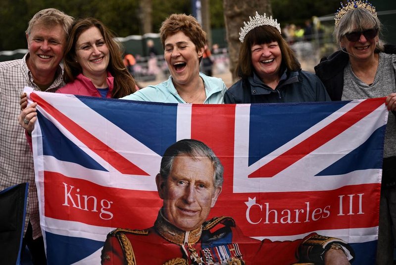 Royal fans pose with a Union Jack flag depicting Britain's King Charles III  along the procession route, on The Mall, near to Buckingham Palace in central London, on May 5, 2023, ahead of the coronation weekend. - The country prepares for the coronation of Britain's King Charles III and his wife Britain's Camilla, Queen Consort on May 6, 2023. (Photo by Marco BERTORELLO / AFP)<!-- NICAID(15420691) -->