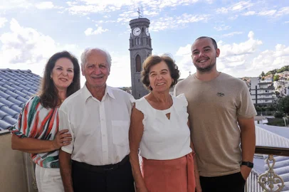 FLORES DA CUNHA, RS, BRASIL, 08/03/2023. o casal Rubem Muraro, 82 anos, e Zelinda Paviani Muraro, 80, com a filha Adriane Muraro Venturini, 57 anos, e o neto Paulo Ricardo Venturini, 26 anos. Matéria sobre a relação dos moradores de Flores da Cunha com o campanário da igreja, o badalar dos sinos e o relógio. Eles têm o campanário da igreja como vizinho há décadas e uma vista privilegiada do prédio onde moram, a poucos metros da Igreja Matriz Nossa Senhora de Lourdes.. Campanário será entregue revitalizado em uma solenidade neste sábado, dia 11.  (Neimar De Cesero/Agencia RBS)Indexador: NEIMAR DE CESERO<!-- NICAID(15369914) -->