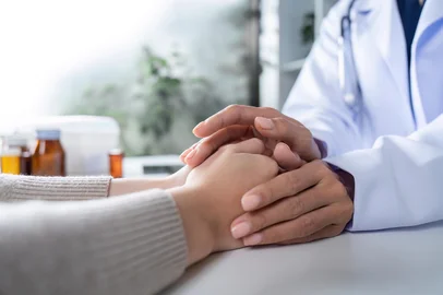 Compassionate Female Doctor Comforting Patient by Holding Hands in a Medical SettingCuidado, carinho, atenção. Foto: wichayada / stock.adobe.comFonte: 1042582119<!-- NICAID(16006781) -->
