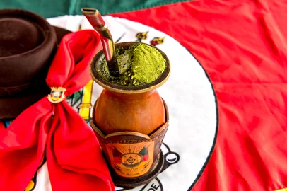 Traditional yerba mate tea, chimarrão gaucho from southern Brazil, Rio Grando do Sul flag in the background. Foto: Giovani Dressler / stock.adobe.comIndexador: Giovani DresslerFonte: 516471721<!-- NICAID(16126951) -->