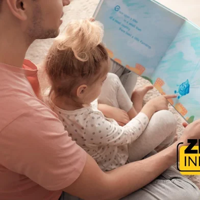 Father and his daughter reading book on floor in children room<!-- NICAID(16198346) -->