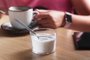 Woman holding a cup of coffee with milk and next to the sweetenerWoman with clock and phone holding a cup of coffee with milk and next to sugar substitute in a cafeIndexador: Vadim ZakirovFonte: 450857808<!-- NICAID(15469635) -->