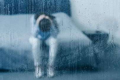 depressed woman sitting on bed and holding head in hands through window with raindropsdepressed woman sitting on bed and holding head in hands through window with raindropsFonte: 249600768<!-- NICAID(15597174) -->