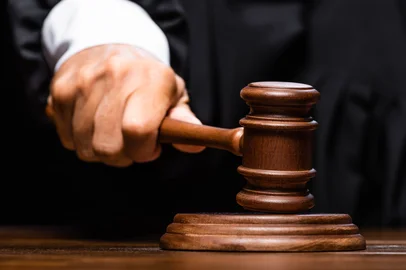 cropped view of judge in judicial robe sitting at table and hitting with gavel