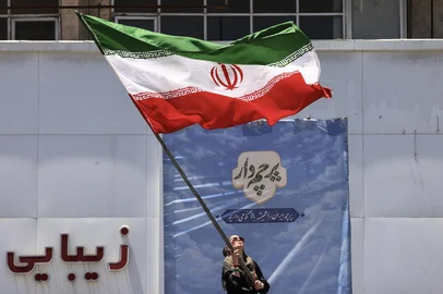An Iranian woman waves a national flag at Valiasr Square in Tehran on June 15, 2026. The United States and Iran agreed a peace deal and an "immediate and permanent" end to military operations on all fronts including Lebanon, mediator Pakistan said, signaling the apparent end to more than three months of war in Middle East. (Photo by ATTA KENARE / AFP) / <!-- NICAID(16308328) -->