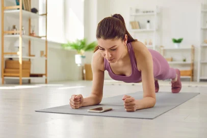 Sporty young woman doing plank exercise on yoga mat and using fitness app on cellphoneBeautiful fit young woman having sports workout at home, doing plank exercise on yoga mat, trying to endure physical exertion and using modern fitness mobile app on her cellular phoneFonte: 617487398<!-- NICAID(15497530) -->