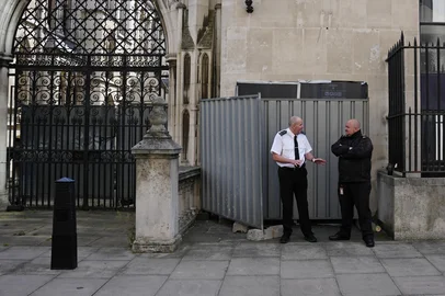 Security guards stand beside a metal barrier covering up an artwork by street artist Banksy, depicting a judge using a gavel to beat a protester using a placard as protection, on an exterior wall of the Royal Courts of Justice in London, on September 8, 2025. (Photo by CARLOS JASSO / AFP)<!-- NICAID(16119524) -->