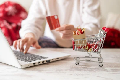 Woman is using laptop and holding credit card, doing online shopping for christmas gifts, with miniature shopping cart full of red decorations in the foregroundWoman is using laptop and holding credit card, doing online shopping for christmas gifts, with miniature shopping cart full of red decorations in the foregroundFonte: 1684636844<!-- NICAID(16188731) -->