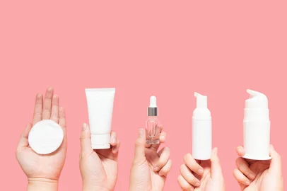 Skincare routine step for healthy skin - Woman hands holding facial cotton pad, foam, essential oil, serum, lotion and eye cream packaging on pink background. Beauty and cosmetic concept. Copy space.<!-- NICAID(16122648) -->