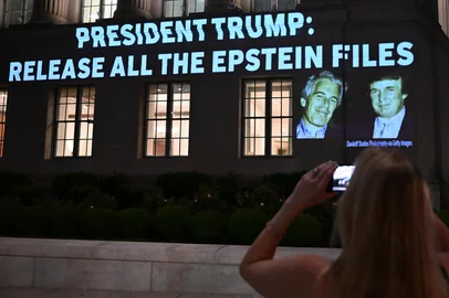 A person takes a photo as a message calling on President Donald Trump to release all files related to Jeffrey Epstein is projected by an activist group onto the US Chamber of Commerce building across from the White House in Washington, DC, on July 18, 2025. President Donald Trump's administration said it would seek the release of grand jury testimony related to Jeffrey Epstein, as the US president sought to dispel lingering political fallout over his team's handling of the late financier's sex trafficking case. Attorney General Pam Bondi said the Justice Department will ask a court to unseal the grand jury transcripts, as Trump's relationship with Epstein came under the spotlight again over an alleged off-color letter published by the Wall Street Journal. (Photo by Alex WROBLEWSKI / AFP)<!-- NICAID(16088257) -->