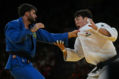 South Korea's Han Ju-yeop and Brazil's Rafael Macedo (Blue) compete in the judo men's -90kg repechage bout of the Paris 2024 Olympic Games at the Champ-de-Mars Arena, in Paris on July 31, 2024. (Photo by Luis ROBAYO / AFP)<!-- NICAID(15828149) -->