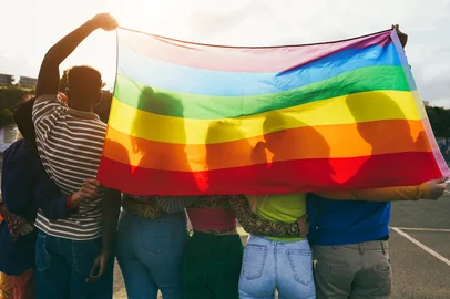 Young diverse people having fun holding lgbt rainbow flag outdoor - Main focus on african guy back<!-- NICAID(16071779) -->