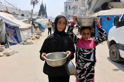 Displaced Palestinians carry pots of lentil soup that they received at a food distribution point in Gaza City in the northern Gaza Strip on July 25, 2025. Aid groups warned of surging numbers of malnourished children in war-ravaged Gaza as a trio of European powers prepared to hold an "emergency call" on July 25 on the deepening humanitarian crisis. (Photo by Omar AL-QATTAA / AFP)Editoria: WARLocal: Gaza CityIndexador: OMAR AL-QATTAASecao: foreign aidFonte: AFPFotógrafo: STR<!-- NICAID(16087941) -->