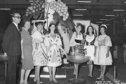 Estande da Vinícola Mosele na Festa da Uva de 1965. Identifica-se da esquerda para a direita: Ottoni Minghelli (Presidente da Festa da Uva), Alice Loman Mosele, Clara Maria Nesi (Princesa da Festa da Uva), Silvia Ana Celli (Rainha da Festa da Uva), Ana Maria Botelho, Maria Paula Pezzi Portela e Martha Campos De Carli (princesas da Festa da Uva).<!-- NICAID(10238534) -->