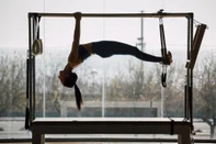 Fit female coach hanging hands and feet from the Pilates machine, woman working out on the Trapeze Table in a big Fitness Gym, big windows and street views. Pilates and healthy lifestyle conceptFonte: 419365360<!-- NICAID(15673409) -->