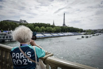 A Paris 2024 volunteer takes a picture on the Invalides bridge next to the tribunes set up on the Seine river on the eve of the Paris 2024 Olympic Games opening ceremony in Paris on July 25, 2024. (Photo by STEPHANE DE SAKUTIN / AFP)<!-- NICAID(15826454) -->