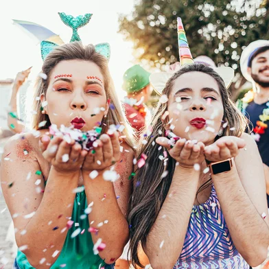 Brazilian Carnival. Young women in costume enjoying the carnival party blowing confettiCarnaval no Brasil. Foto:  kleberpicui / stock.adobe.comFonte: 307105889<!-- NICAID(15352476) -->