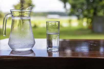 A jug of water and a glass of cold water are placed on a wooden table against a beautiful backdrop.<!-- NICAID(16267471) -->