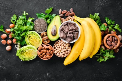 Adobe Stock - MagnésioFoods containing natural magnesium. Mg: Chocolate, banana, cocoa, nuts, avocados, broccoli, almonds. Top view. On a black background.Fonte: 251835187<!-- NICAID(16095611) -->