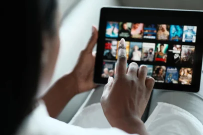 Black Woman Browsing Movie On Streaming Media ServiceAfrican American Woman Lying Down On Sofa At Home, Choosing Movie On Internet Streaming Service. Over The Shoulders.Fonte: 349411371<!-- NICAID(15501618) -->