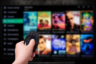 Multimedia streaming concept. Hand holding remote control. TV screen with lot of pictures. VoD content provider<!-- NICAID(15995526) -->