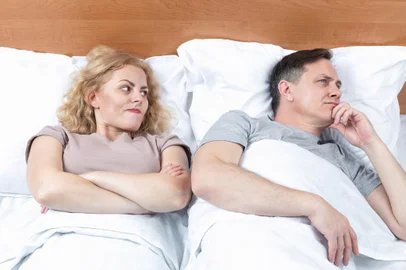Two in bed, a woman looks with suspicion at a man who has turnedFonte: 473536900<!-- NICAID(15472593) -->