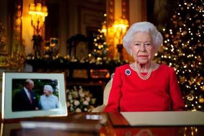A picture released on December 23, 2021 shows Britain's Queen Elizabeth II posing for a photograph as she recorded her annual Christmas Day message, with a photograph of herself and her late husband Britain's Prince Philip, Duke of Edinburgh, taken in 2007 at Broadlands, to mark their Diamond Wedding Anniversary, in the White Drawing Room Windsor Castle, west of London. (Photo by Victoria Jones / POOL / AFP) / EMBARGOED UNTIL 2230 GMT on December 23, 2021.<!-- NICAID(14976580) -->