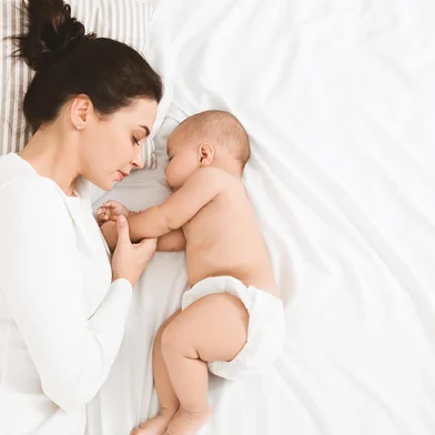 Bedtime. Adorable baby sleeping with his mother in bed, touching hands, top view, copy space. <!-- NICAID(16048333) -->