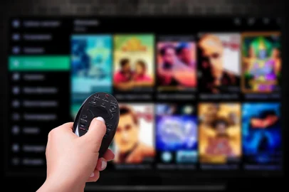 Multimedia streaming concept. Hand holding remote control. TV screen with lot of pictures. VoD content provider<!-- NICAID(15995526) -->