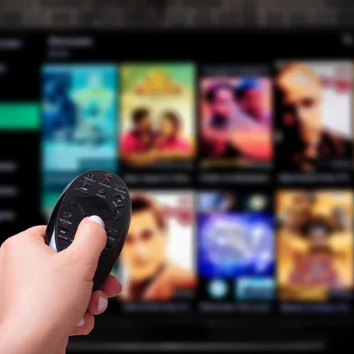 Multimedia streaming concept. Hand holding remote control. TV screen with lot of pictures. VoD content provider<!-- NICAID(15995526) -->