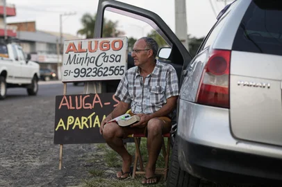 TORRES, RS, BRASIL, 17-01-2026: Júlio de Mesquita Bernardino, 59 anos, ao lado da placa em que oferece sua casa para alugar. Moradores de Torres, no Litoral Norte, aguardam à beira da estrada que dá acesso à cidade com placas para alugar suas próprias casas durante a temporada de verão. A prática, tradicional na cidade, leva famílias a deixarem temporariamente suas residências nesse período, algumas passam a viver na casa de parentes ou em pequenos cômodos anexos, para obter renda extra com veranistas que chegam de última hora. Foto: Mateus Bruxel/Agência RBSIndexador: MATEUS BRUXEL<!-- NICAID(16207488) -->