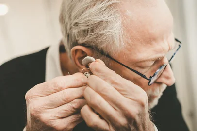 Senior man putting hearing aidsFonte: 290457223<!-- NICAID(15431539) -->