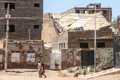 A woman and a child walk past a damaged building in the capital Khartoum on April 15, 2026, on the third anniversary of the start of the war between the army and its paramilitary foes. On the third anniversary of the start of the grinding conflict on April 15, donors will gather in Berlin for an international conference aimed at reviving faltering peace talks and mobilising aid for one of the world's worst humanitarian crises. (Photo by Ebrahim Hamid / AFP)<!-- NICAID(16266234) -->