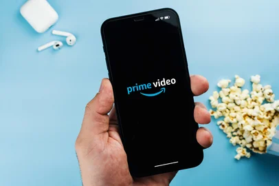 Man holding a smartphone with Amazon Prime Video streaming app on the screen. Blue background with popcorn and AirPods. Rio de Janeiro, RJ, Brazil. April 2022.Fonte: 500991784<!-- NICAID(15984463) -->