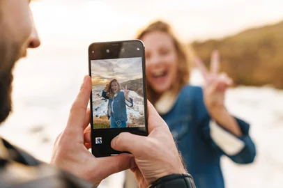 Image of beautiful young caucasian couple taking photo on cellphone while walking by seaside<!-- NICAID(15899494) -->