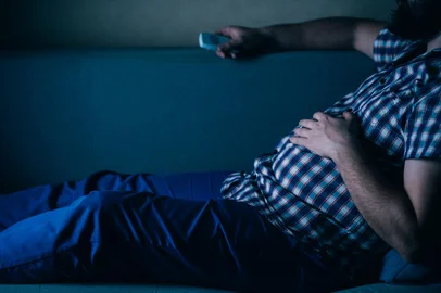 overweight man with tv remote on the coachSsedentarismo. Foto: Vadym / stock.adobe.comFonte: 320191421<!-- NICAID(15798394) -->