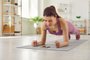 Sporty young woman doing plank exercise on yoga mat and using fitness app on cellphoneBeautiful fit young woman having sports workout at home, doing plank exercise on yoga mat, trying to endure physical exertion and using modern fitness mobile app on her cellular phoneFonte: 617487398<!-- NICAID(15497530) -->