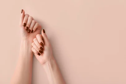 Female hands with beautiful brown manicure on light backgroundFonte: 514386711<!-- NICAID(15748959) -->