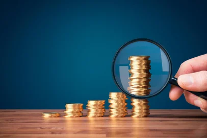 Money makes money investment concept with magnifying glass. Coins in shape of growing graph and focus on the biggest column.<!-- NICAID(15629805) -->