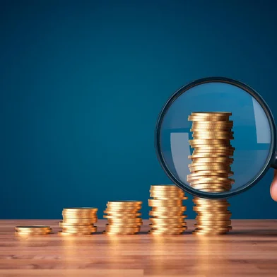 Money makes money investment concept with magnifying glass. Coins in shape of growing graph and focus on the biggest column.<!-- NICAID(15629805) -->