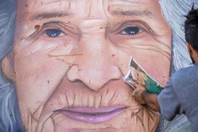 Pintura do mural retratando dona Tarcilia Vieira Rodrigues, a dona Cia, moradora mais antiga do bairro Euzébio Beltrão de Queiroz, em Caxias do Sul. Ela nasceu em 5 de junho de 1929 e completa 94 anos nesta segunda.Desenvolvida pelos artistas Erick Citron, Ana Scarceli e Leandro Alves, a obra fica no acesso à casa de dona Tarcília e integra o projeto Muros da Quebrada edição 2, que tem financiamento da Lei de Incentivo à Cultura de Caxias do Sul. A realização é do Instituto Samba, com apoio institucional Chiquinho Divilas e Vielas Espaço Cultural e apoio cultural da Orquídea e Agrale SA. Na foto, Erick Citron com a fotografia de dona Cia que inspirou a pintura.<!-- NICAID(15441814) -->