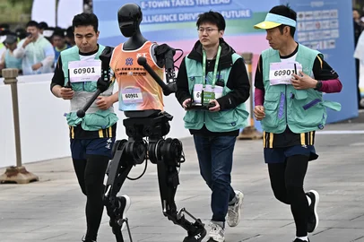 A robot and its engineers run in the humanoid robot half marathon in Beijing on April 19, 2025. Dozens of humanoid robots took to the streets of Beijing, joining thousands of their flesh-and-blood counterparts in a world-first half marathon showcasing China's drive to lead the global race in cutting-edge technology. (Photo by Pedro PARDO / AFP)Editoria: SCILocal: BeijingIndexador: PEDRO PARDOSecao: science (general)Fonte: AFPFotógrafo: STF<!-- NICAID(16020333) -->