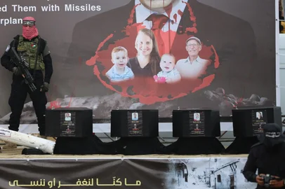 A Palestinian militant group Hamas fighter stands on stage next to the coffins of the four Israeli hostages ahead of the handing them over to the Red Cross in Khan Yunis in the southern Gaza on February 20, 2025. Hamas is due to hand over the bodies of four hostages on February 20, including those of the Bibas family, who have become symbols of the hostage crisis that has gripped Israel since the Gaza war broke out. The transfer of the bodies is the first such handover of remains by Hamas since its October 7, 2023 attack on Israel triggered the war. (Photo by Eyad BABA / AFP)<!-- NICAID(15980153) -->