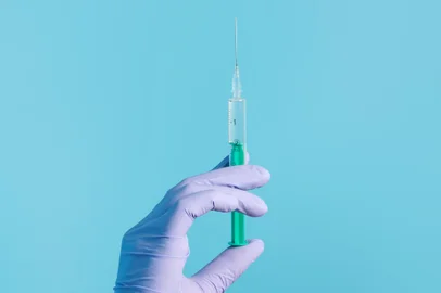 Snejana / stock.adobe.com Syringe for injection in hand, latex medical gloves on hand. On a blue background.Seringa, luva, injeção, mão. Foto: Snejana / stock.adobe.comFonte: 408254657<!-- NICAID(14840403) -->