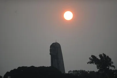 CAXIAS DO SUL, RS, BRASIL, 10/09/2024. Fumaça das queimadas encobre o céu em parte do Brasil e deixa o Sol avermelhado, inclusive no RS. Apesar de não haver nuvens, vestígios dos incêndios impedem a passagem total dos raios solares. Mesmo com tempo ensolarado em alguns regiões, dias estão cinzentos e com aspecto de nublado. Na foto, vistas gerais de Caxias. Pôr do sol, céu cinzento. Silhueta monumento Jesus Terceiro Milênio. (Porthus Junior/Agência RBS)<!-- NICAID(15862804) -->