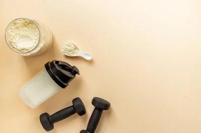 Protein powder in jar and scoop for sports nutrition with black dumbbells, top viewProteína em pó, nutrição. Foto: 9dreamstudio / stock.adobe.comFonte: 1065561035<!-- NICAID(15983477) -->