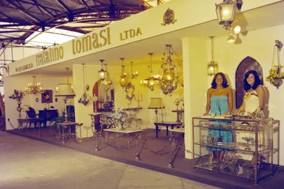 Febre nas residências dos anos 1960, 1970 e 1980, as peças produzidas pela Metalúrgica Natalino Tomasi até hoje são facilmente identificadas, assim como as da Eberle e as do lendário Artesanato Nigavel. Lustres, lampiões, candelabros, luminárias, mesas de cabeceira, cadeiras, castiçais, incensários, fruteiras, abajures, espelhos, arandelas, apliques, porta-retratos, porta-bíblias e uma infinidade de artefatos em metal podiam ser encontrados em diversas lojas de Caxias e região.A apurada técnica do “artesanato em bronze retocado a mão” de Natalino Tomasi também costumava ser exposta na Festa da Uva. Legenda: estande da Metalúrgica Natalino Tomasi na Festa da Uva de 1978, junto aos Pavilhões.<!-- NICAID(16224986) -->